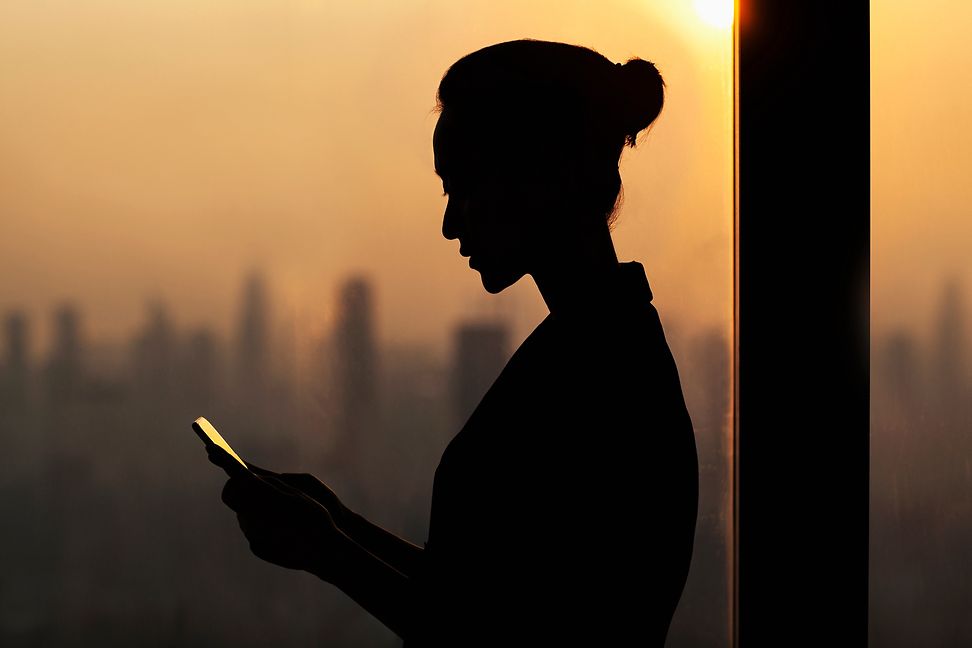 Frau am Handy, vor einer Skyline stehend