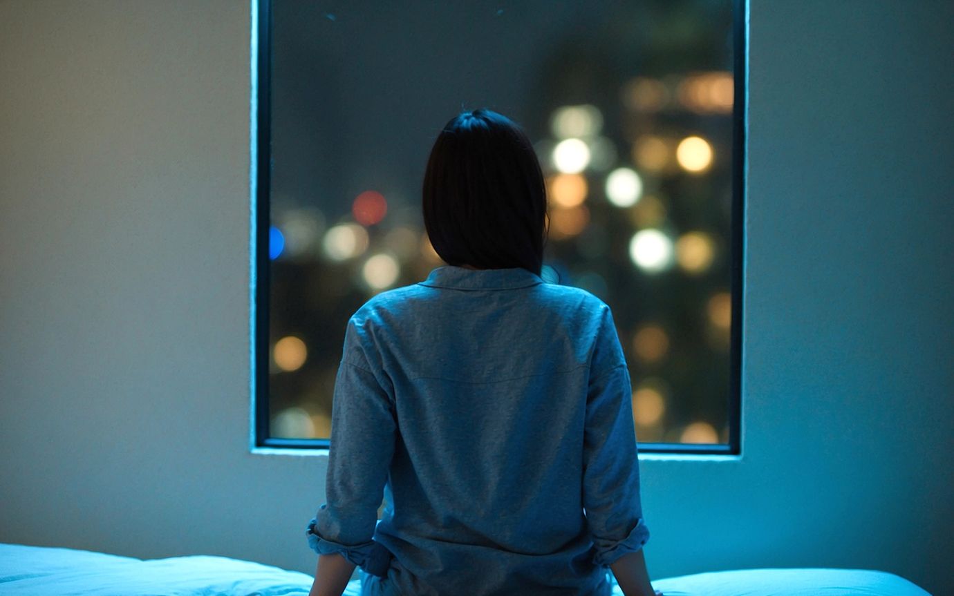 Woman sits on bed at night and looks out of the window