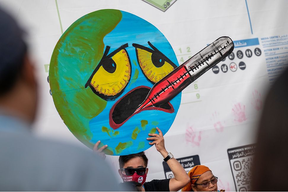 Protestierender hält Cartoon einer Erde hoch, die unter hoher Temperatur leidet, als hätte sie Fieber