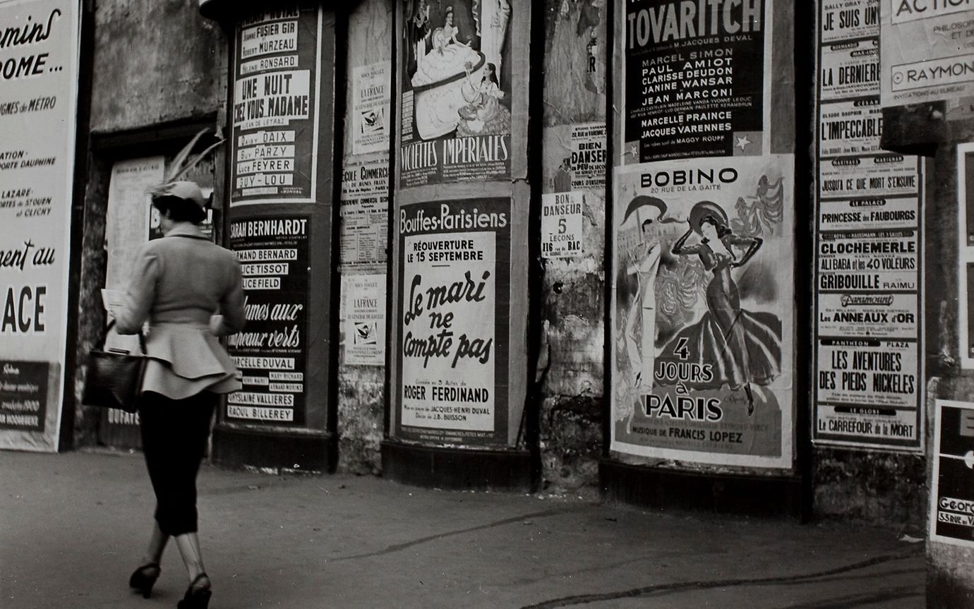 Black and white photo of a woman in front of posters in the 1950s