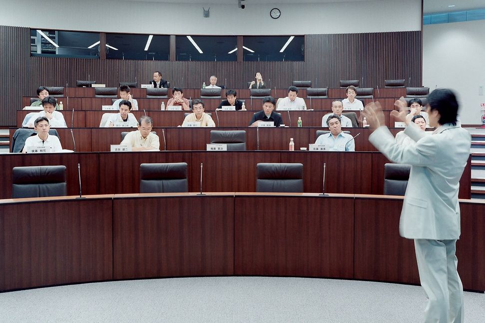 Asian man in a light-coloured suit lectures in an auditorium in front of a group consisting mainly of male business people.