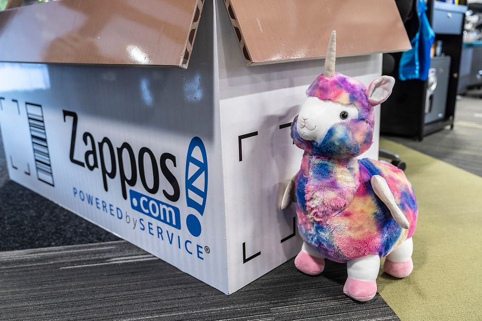 A shipping box stands on a table with a colourful plush sheep next to it. 