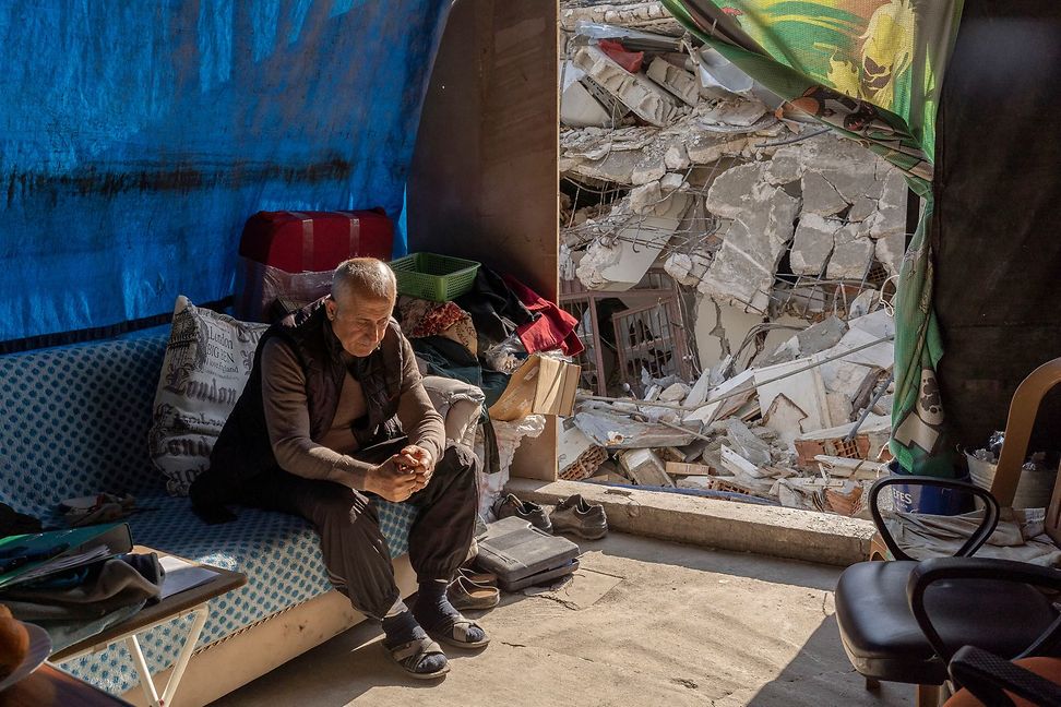A man sits in the rubble of a house after an earthquake.