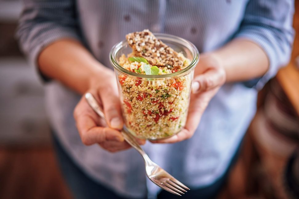 Someone holds a glass of quinoa salad in their hands