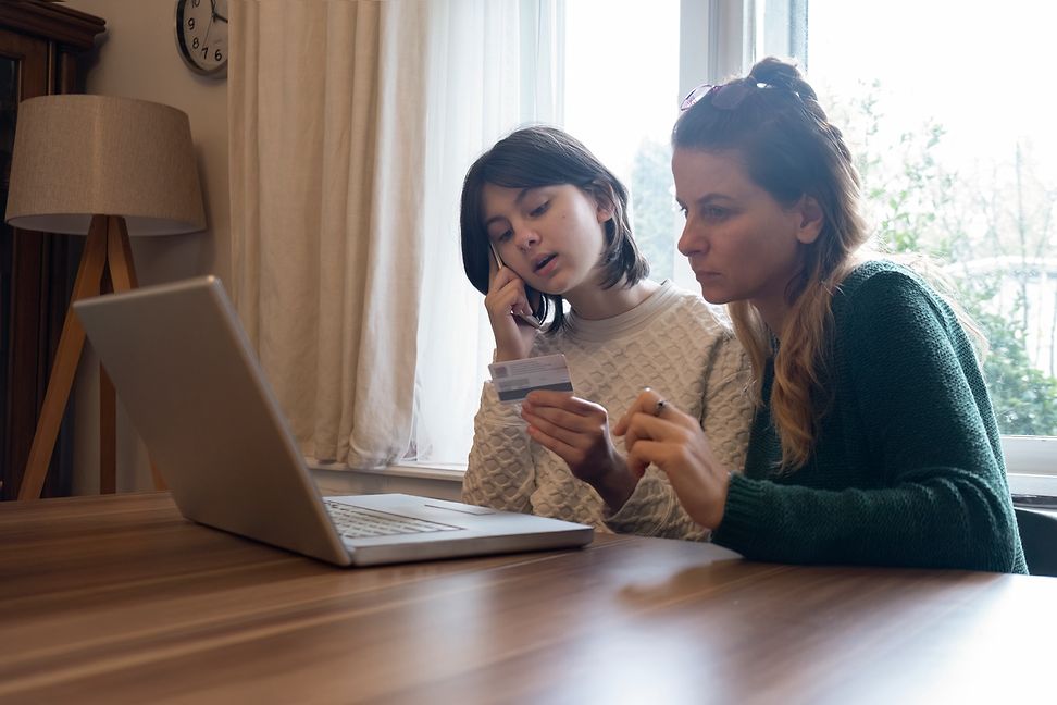 A woman and a child are looking at the screen of a laptop together, the child is holding a credit card.