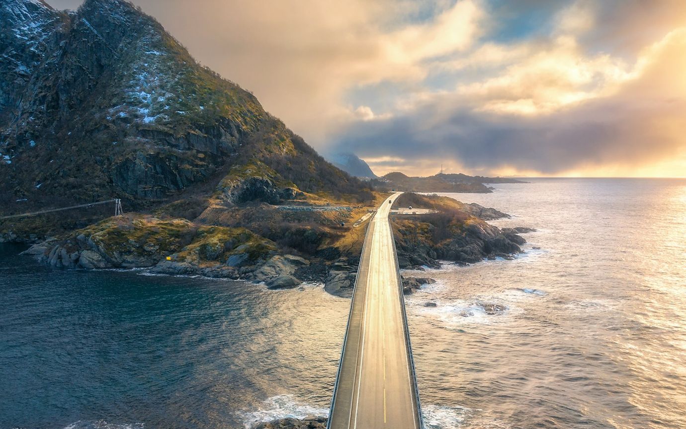 A bridge spans the water in a hilly landscape by the sea.