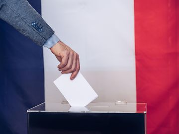 hand places card in ballot box with French flag behind