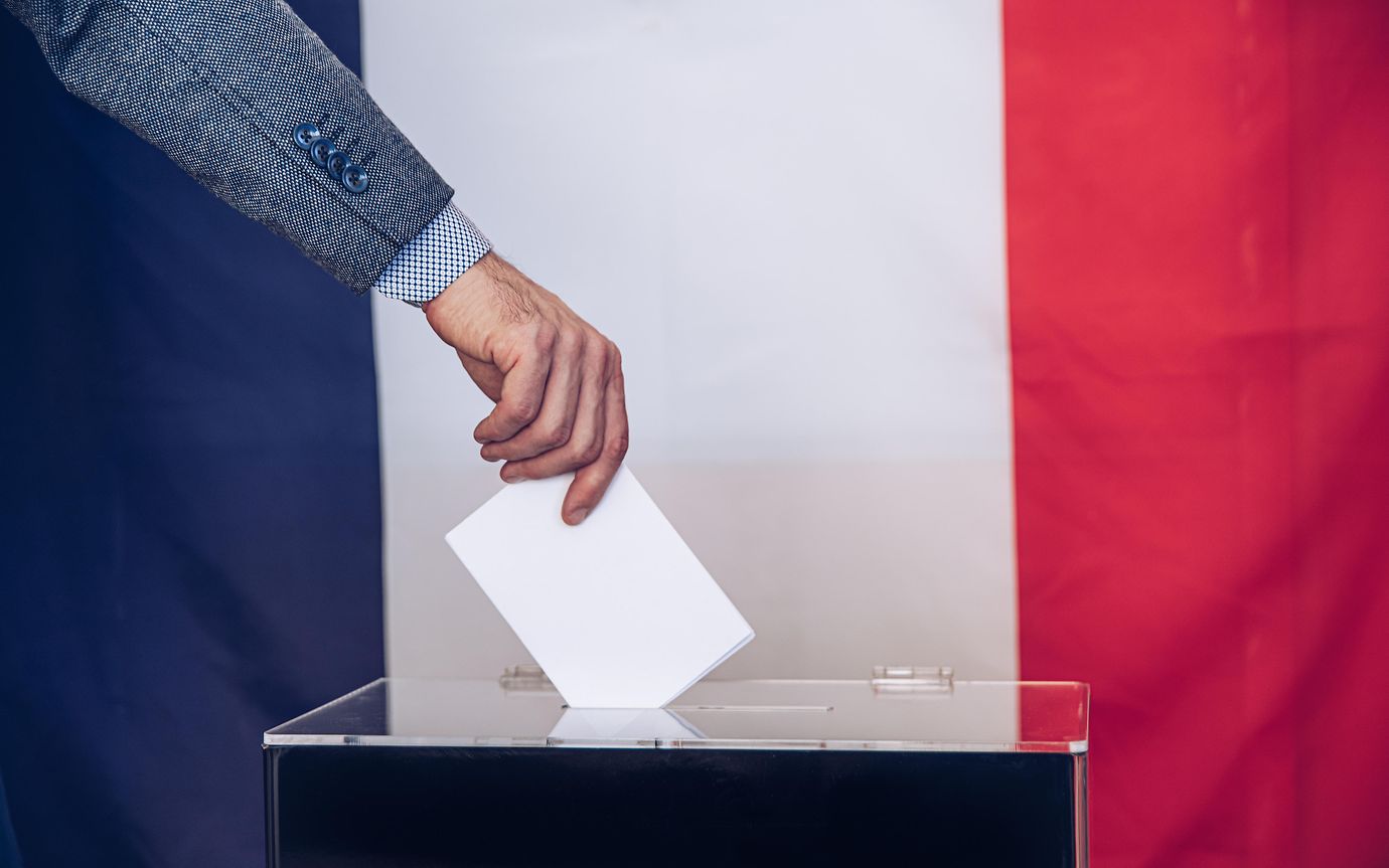 hand places card in ballot box with French flag behind