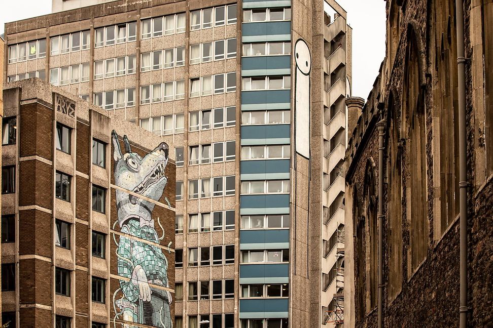 Street Art; auf einem Gebäude ist ein Wolf gemalt, auf dem anderen ein Mensch, sie schauen einander an