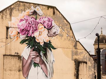 Street art; a woman holds a bouquet of flowers in front of her face