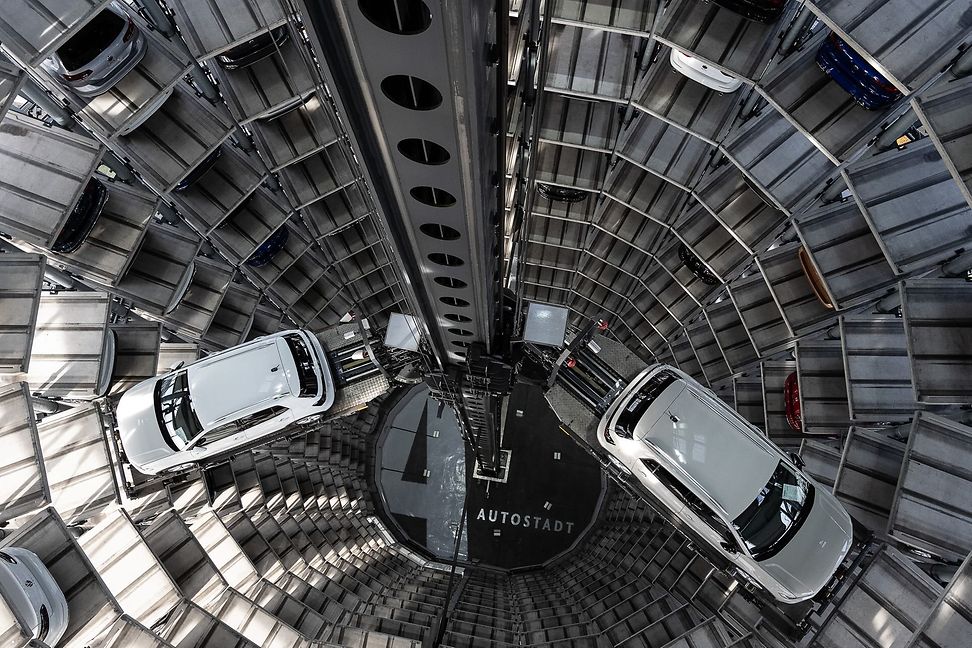 Bird's eye view of the interior of a massive, multi-storey round tower filled with new cars.