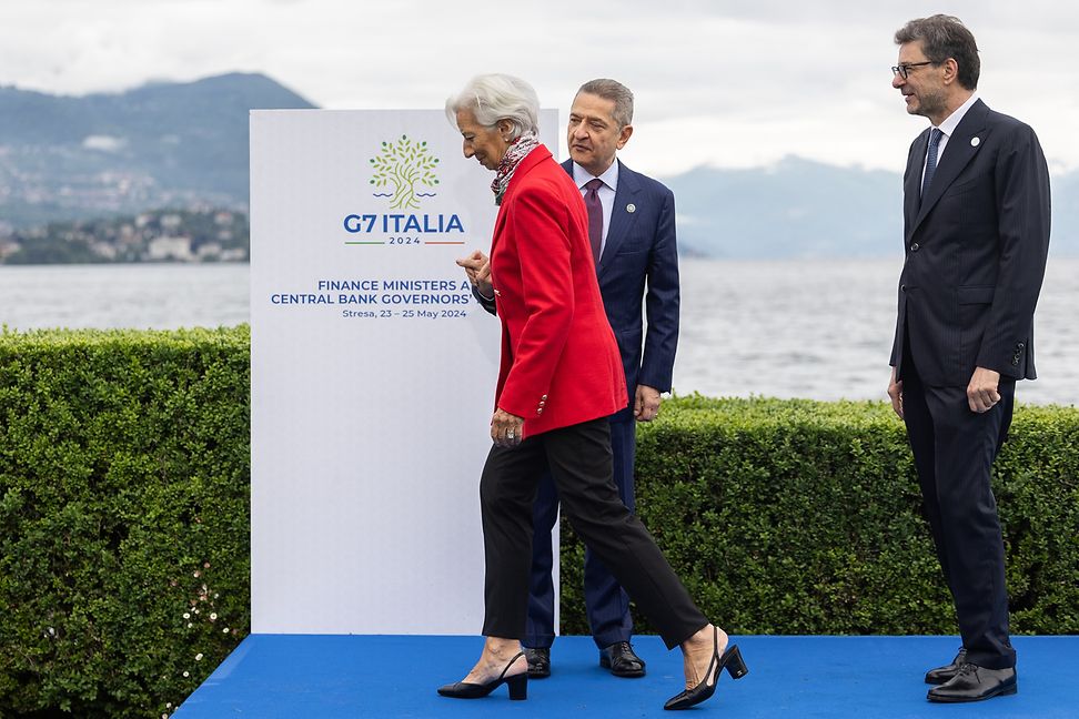 Eine Frau betritt vor zwei Männern ein Podium, vor einem Banner mit der Aufschrift G7 in Italien