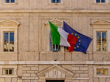 A close-up of an older, official building with the Italian and EU flags.