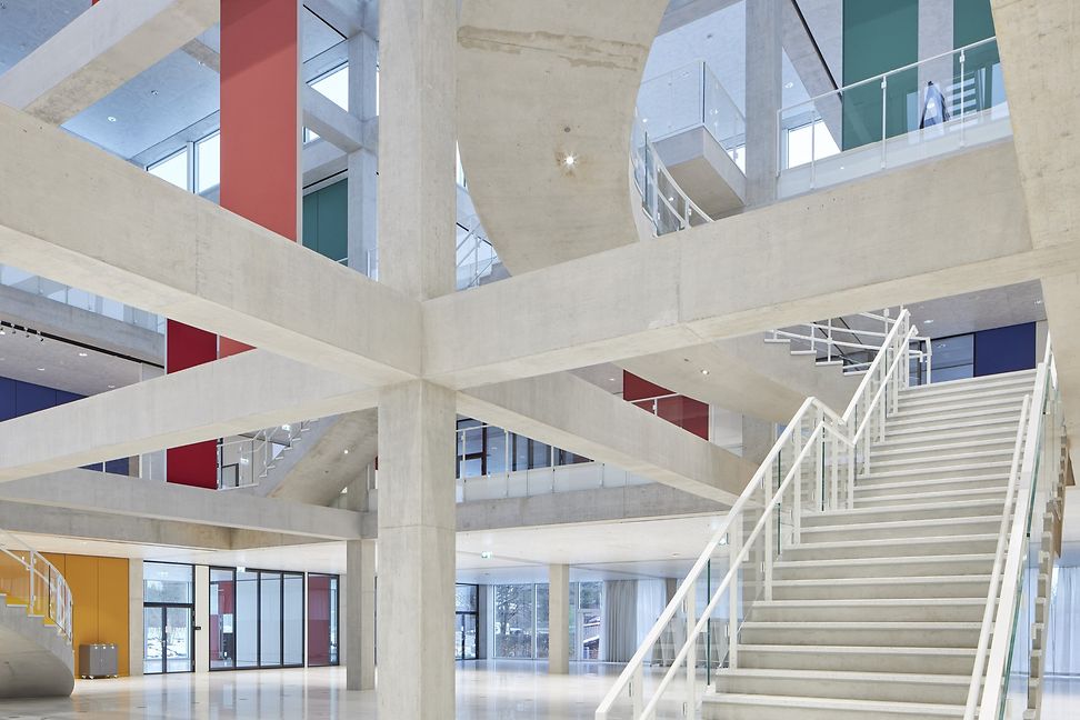 Moderne, helle Architektur einer grösseren Halle, sichtbar sind weisse tragende Balken und eine Treppe. 