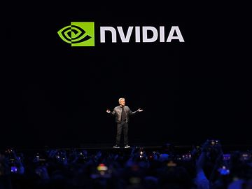 Ein Mann spricht auf einer dunklen Bühne vor dem Schriftzug "Nvidia".