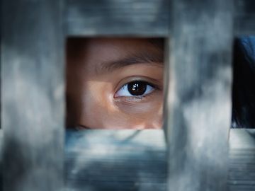A child's eye looks out from a wooden frame.