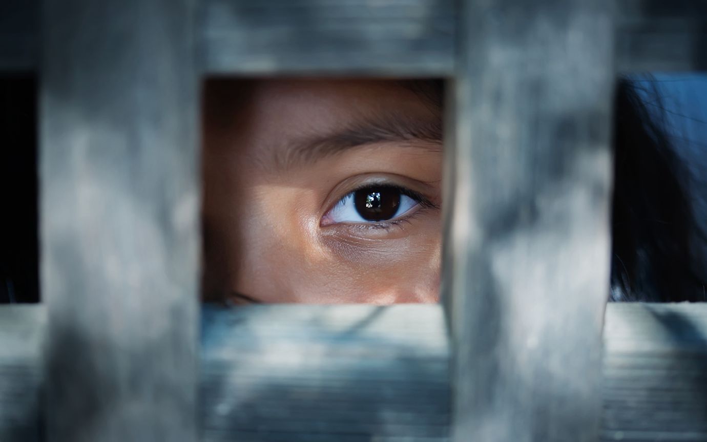 A child's eye looks out from a wooden frame.