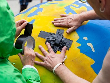 Zwei Aktivistinnen kleben ein Pflaster auf einen Ballon, der aussieht wie eine Erde 