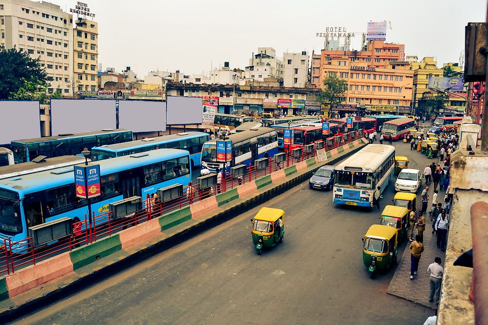 Bus station with several blue buses and rickshaws in an urban setting 