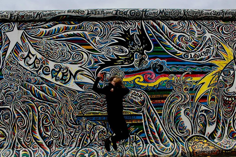 Black wall with white graffiti, a person jumps in front of it.