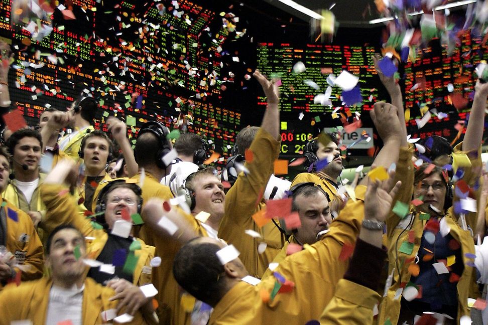 People in yellow suits raise their arms in a shower of confetti. In the background, large screens display rows of numbers 