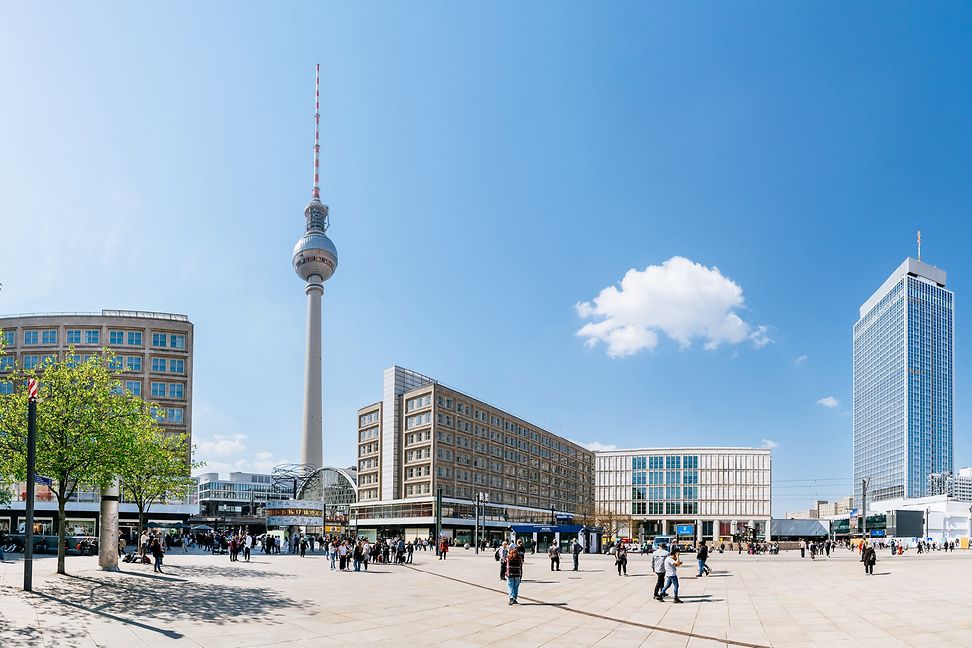 Beyond a large urban square, skyscrapers and a television tower rise against a bright blue sky.