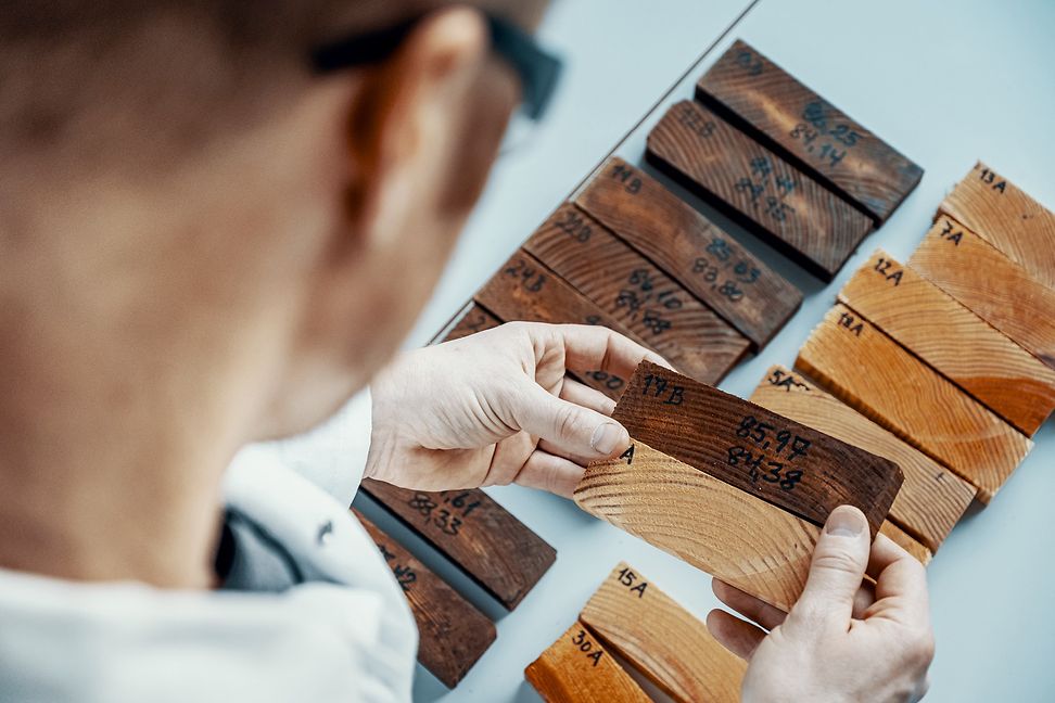 Over the shoulder of a person you can see their hands picking out two pieces of wood from a row, one is darker