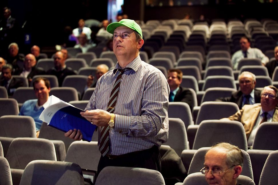 A man in a shirt, tie and baseball cap, a notebook in his hand