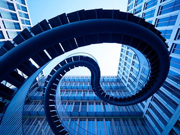 View from below of a winding staircase leading up between tower blocks.