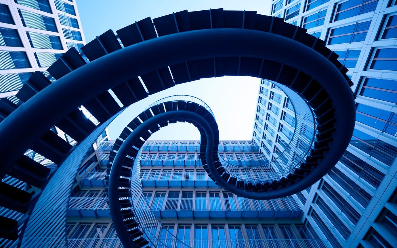 View from below of a winding staircase leading up between tower blocks.