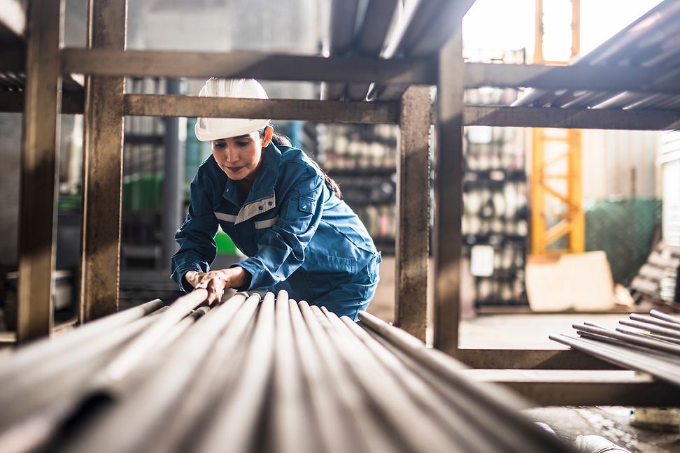 Eine Person mit Helm und Schutzkleidung hantiert in einer Industriehalle mit grossen Rohren.