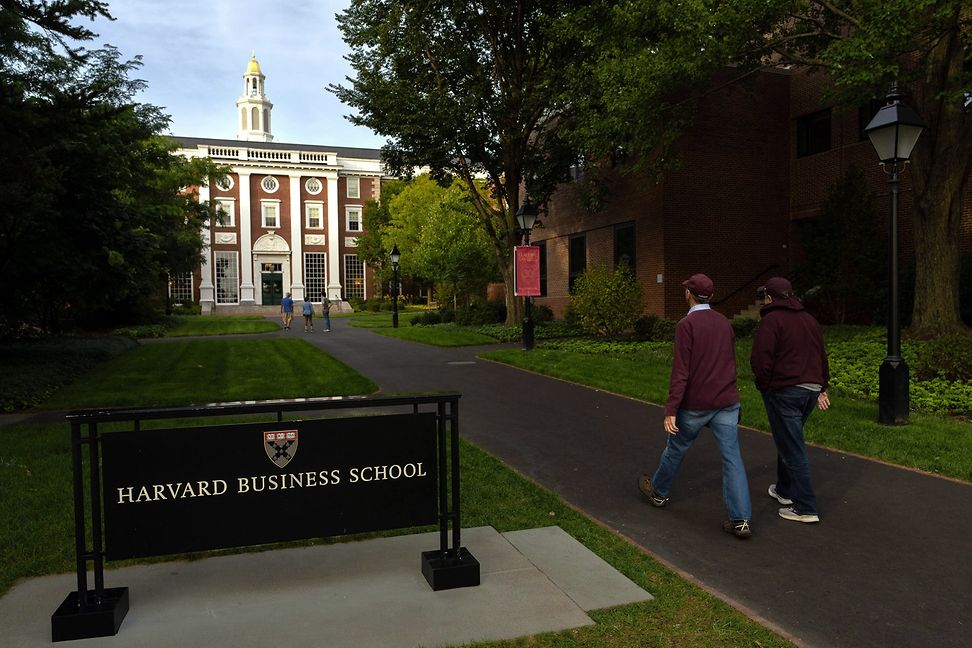 Menschen gehen auf ein Backsteingebäude zu, vor dem ein Schild mit der Aufschrift "Harvard Business School" steht.