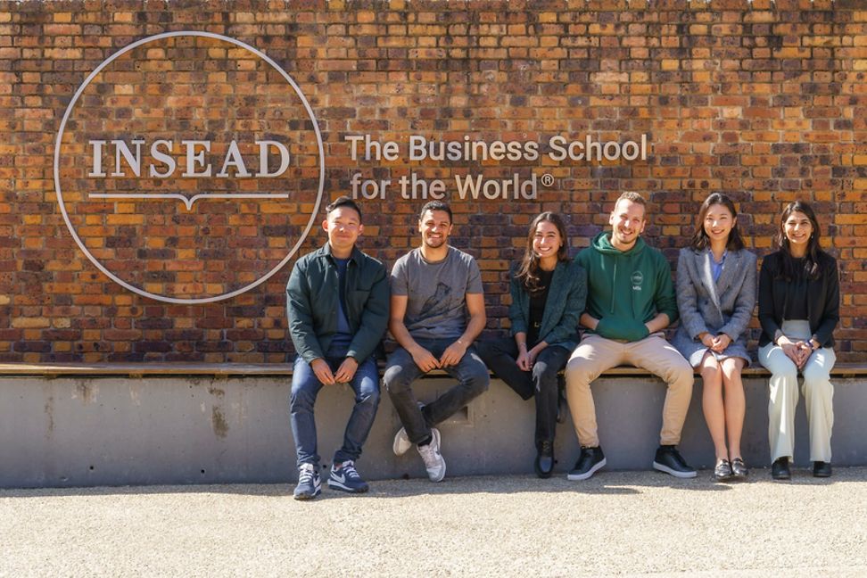 Menschen sitzen vor einer Backsteinmauer, auf der INSEAD steht.