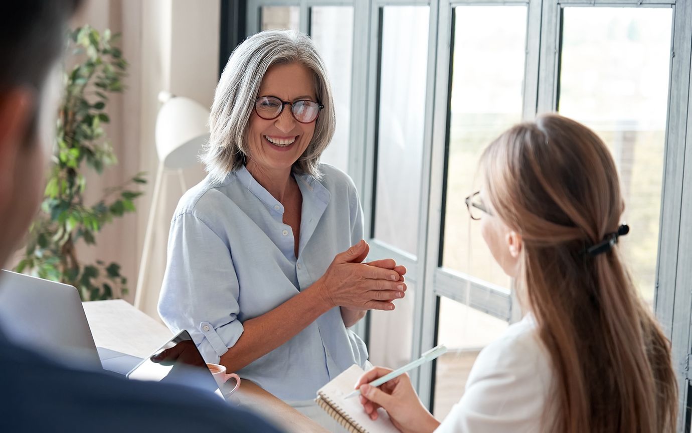 An older woman and a younger person with a notebook are exchanging ideas.