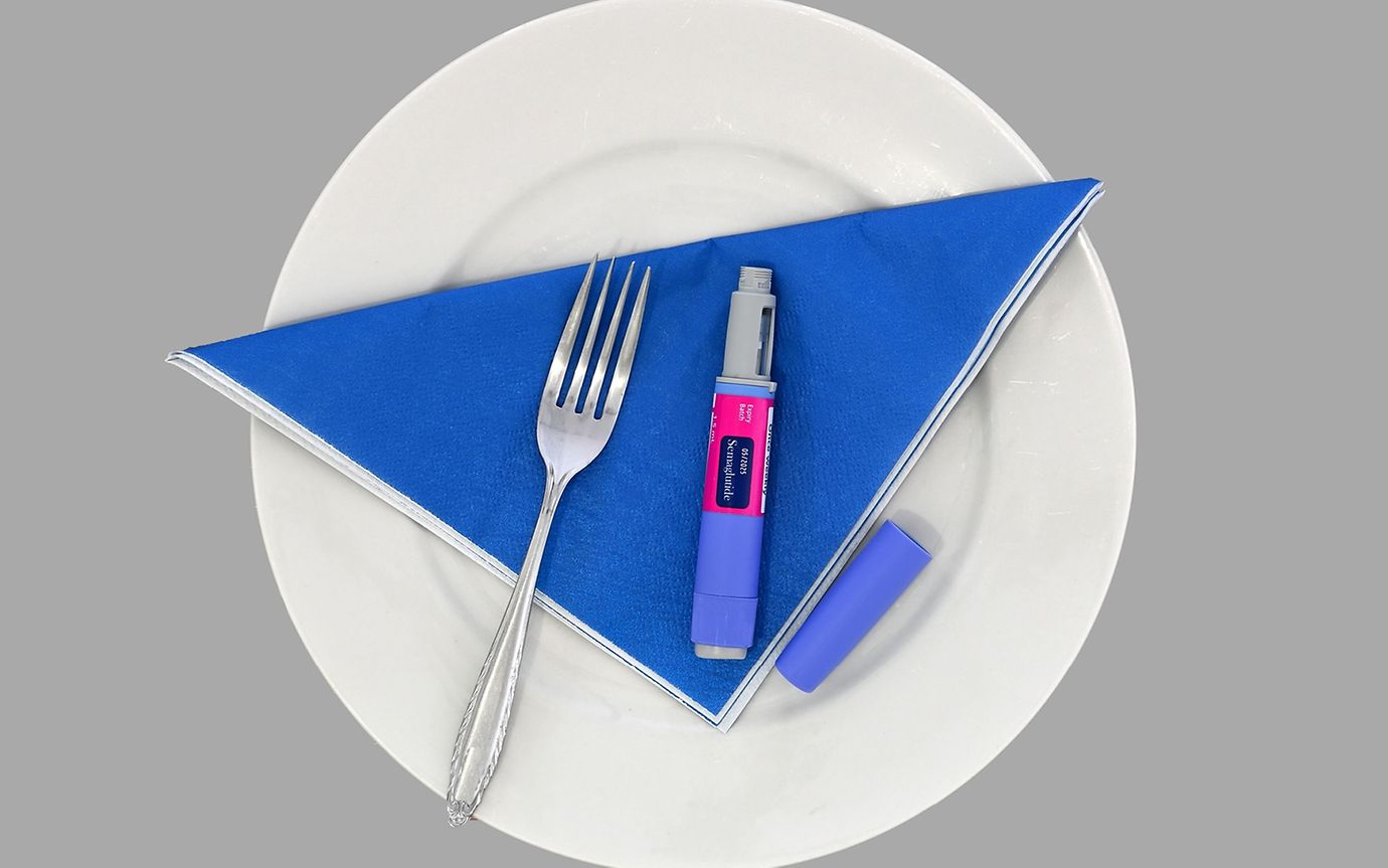 A white plate with a fork and a medicine pen on a blue napkin.