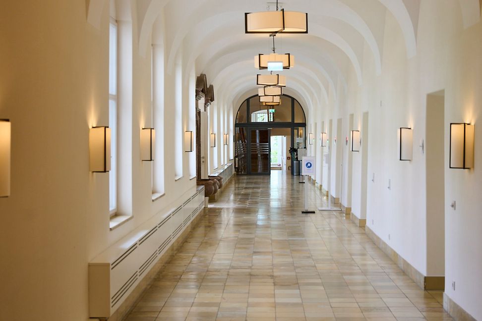 A long corridor with light brown and grey tiles and vaulted ceiling is lit by wall and ceiling lights.