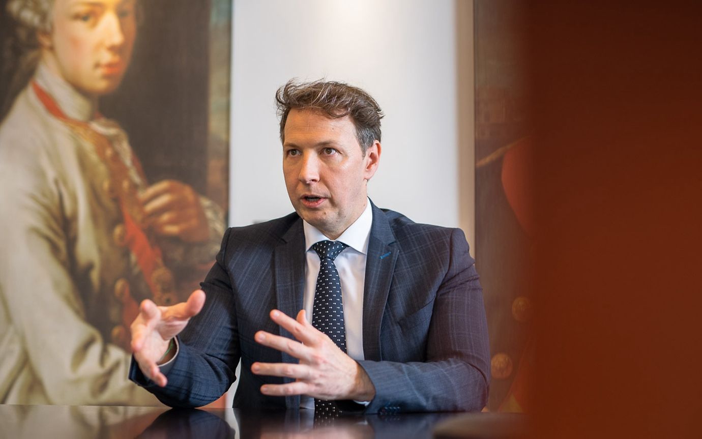 A man in a suit and tie in an office environment talks and gestures with his hands