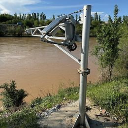 A metal column on the banks of brown river surrounded by forest.