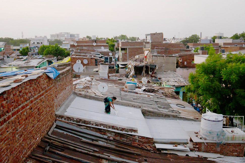 A woman on the roof of a house in a slum, painting it white.