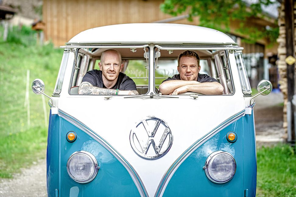 An old version of the famous Volkswagen bully van, painted lightblue and white is parked in the countryside