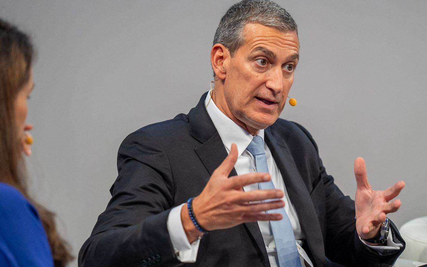 A middle-aged man with dark grey hair, wearing a dark suit, white shirt and light blue tie