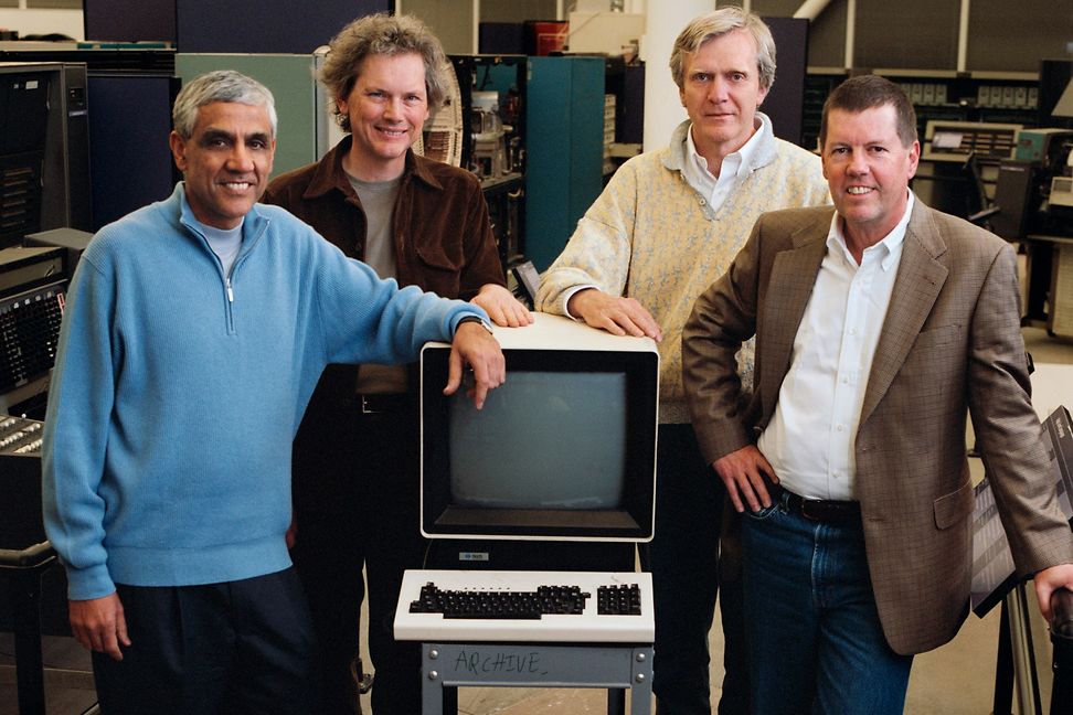 Four men are standing around an old-fashioned computer.