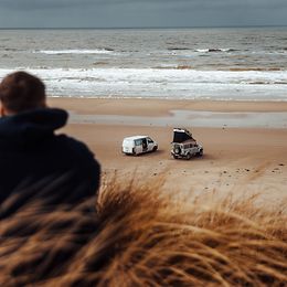 Two caravans are parked on a deserted stretch of beach. In the foreground