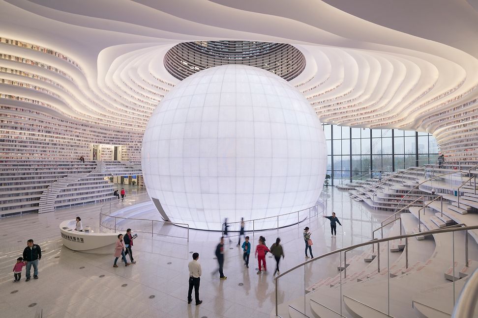 Futuristic library with a central luminous sphere, undulating walls and terraced bookshelves.