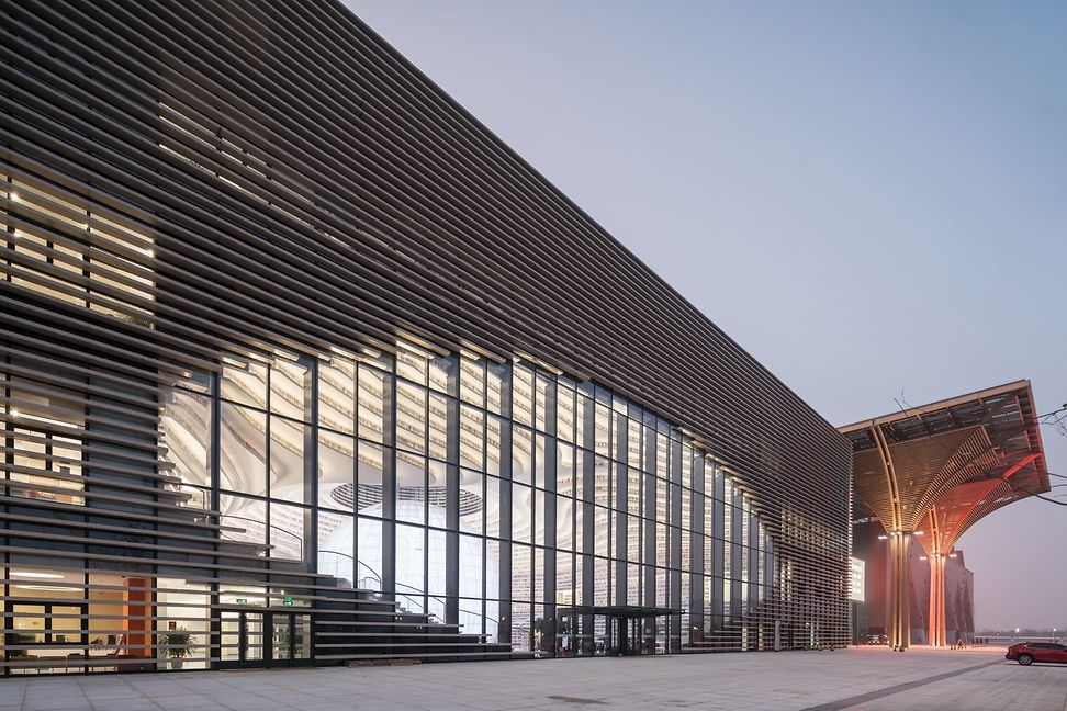 A modern building with glass surfaces and horizontal louvres. An illuminated sphere can be seen inside through the glass front.