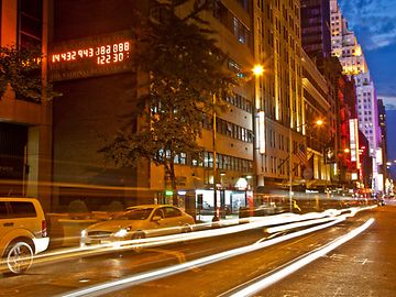 On a busy street in a big city at night, an electronic display shows a series of numbers.