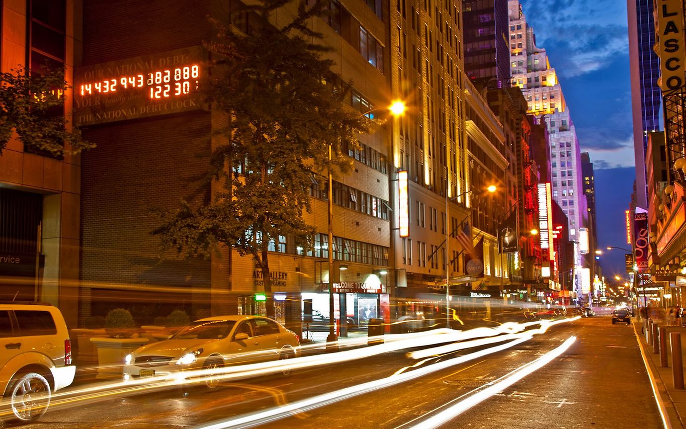 On a busy street in a big city at night, an electronic display shows a series of numbers.