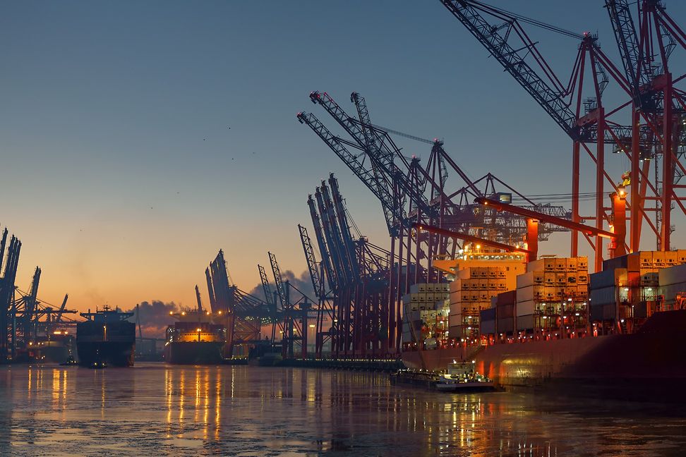 Hafenkrane und Einrichtungen zum Be- und Entladen von Gütern leuchten nachts in einem grossen Hafen.