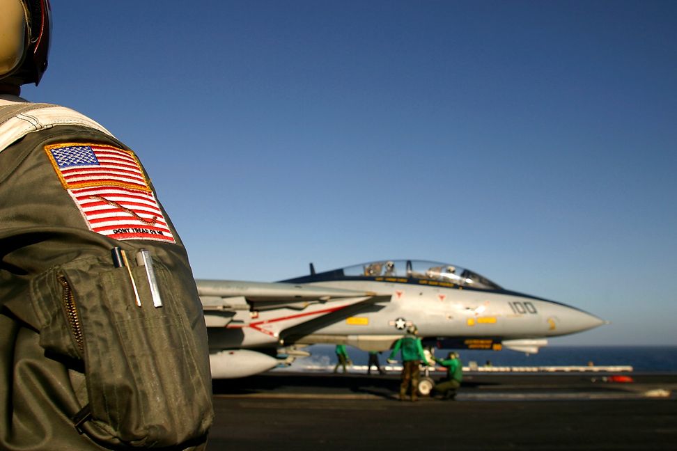 A fighter jet on the runway, seen over the shoulder of a soldier.