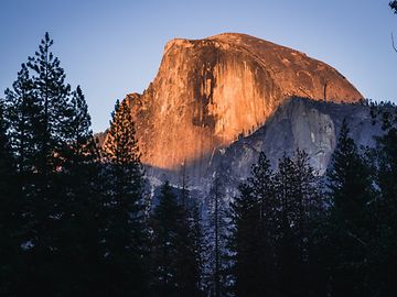 A dome-shaped mountain rises from the forest, with blue sky in the background.